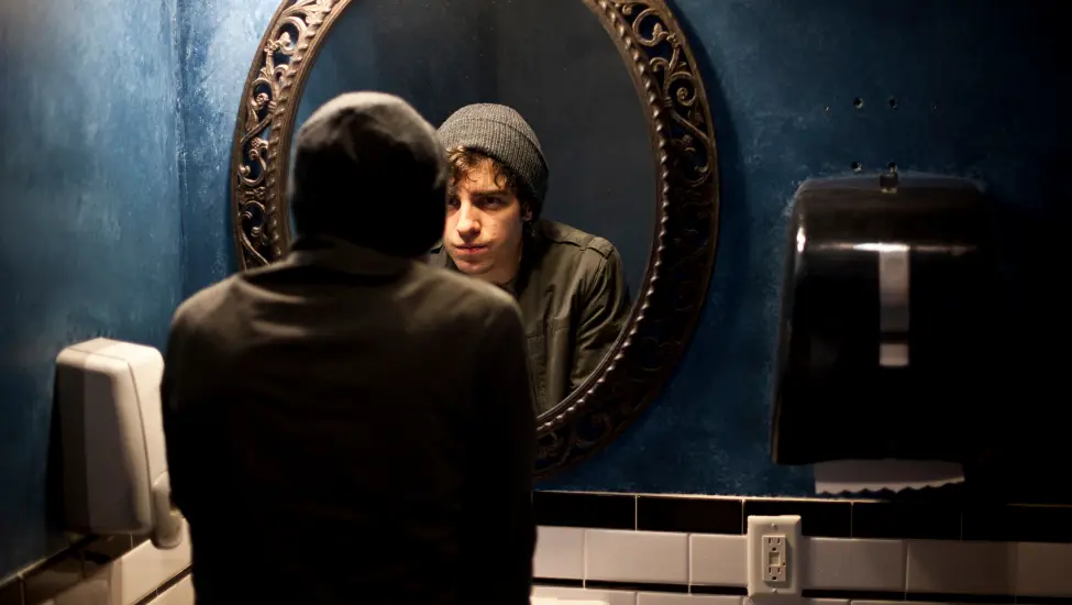 Man in hoodie admiring himself in the bathroom mirror