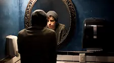 Man in hoodie admiring himself in the bathroom mirror