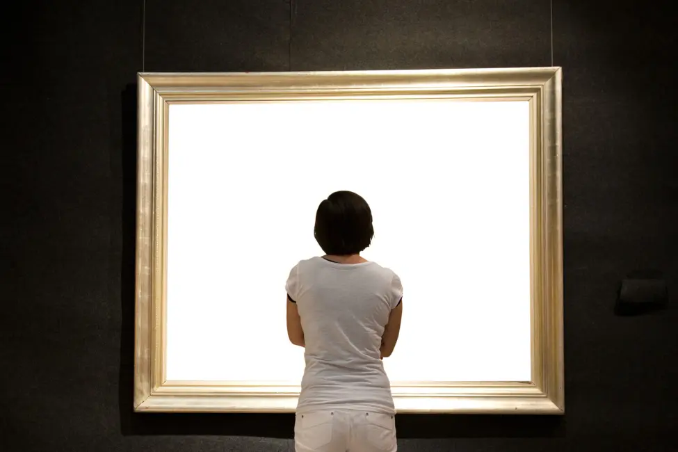 Thoughtfull woman admiring a bright white painting in a classical gold frame