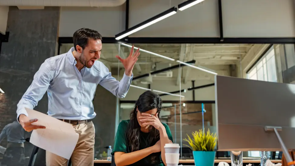 Angry man standing over a women with her head in her hands while he shouts at her