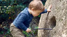 Young child prodding a hole in a rock with a stick