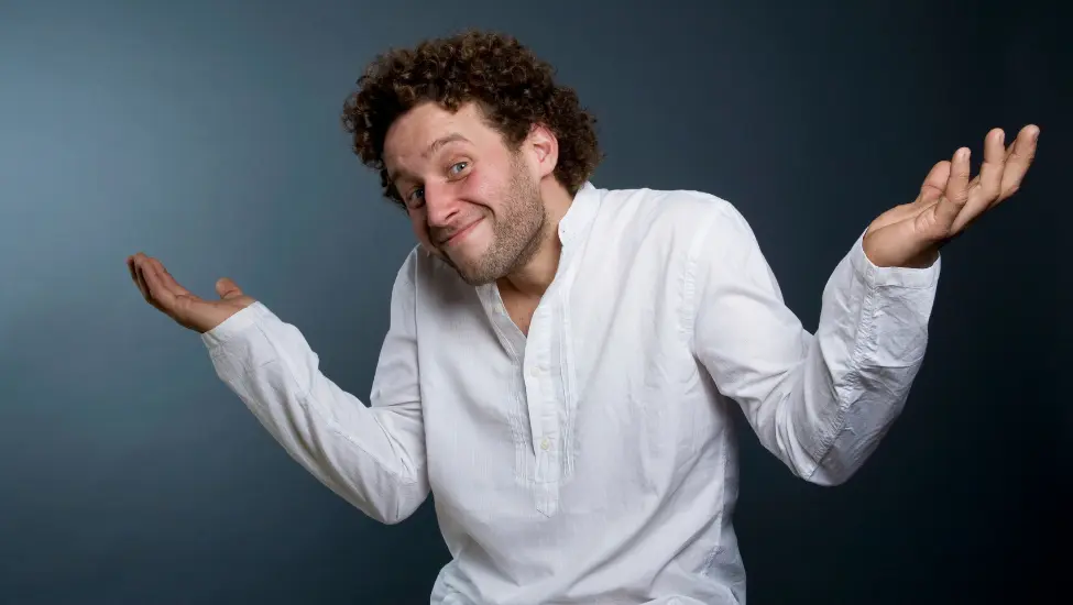 Man in white share with outstretched arms shrugging his shoulders