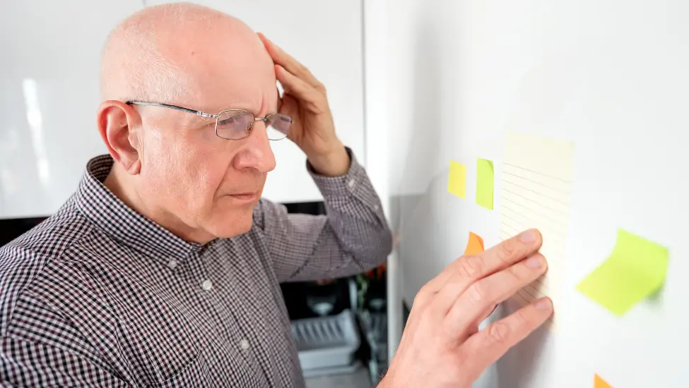older man holding his head looking at post it notes on the fridge
