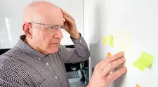 older man holding his head looking at post it notes on the fridge