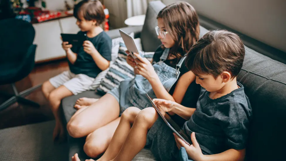 three children sat on the sofa reading on their tablets