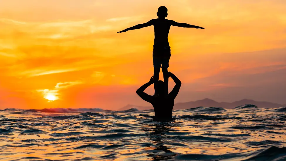 standing on the shoulders of a person in the sea with a golden sunset