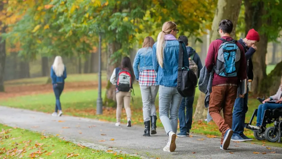 students walking through a park carrying backpacks and books