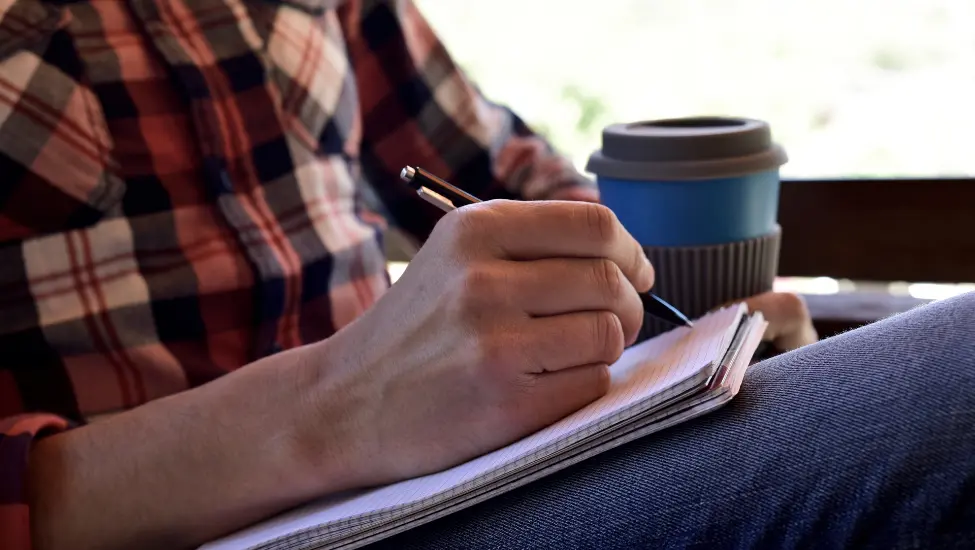Writing on a notepad and drinking a coffee from a paper cup